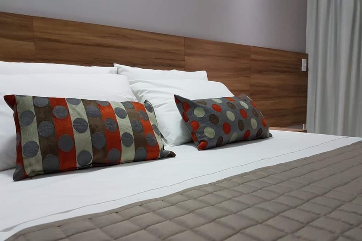 Una cama con sábanas blancas, dos almohadas estampadas y una colcha acolchada.