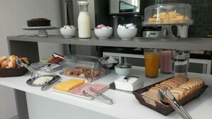 Montaje de bufé con diversos alimentos, como pasteles, frutas y un pastel, además de bebidas y salsas.