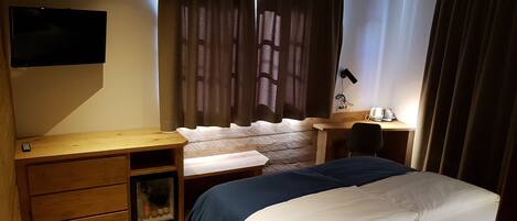 Un dormitorio con cama, escritorio, silla, televisor y ventana con cortinas.