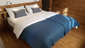 Una cama con ropa de cama blanca y azul, cabecera de madera, lámparas de noche y suelo de madera.