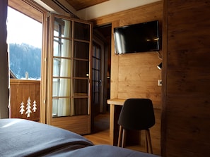 A room with a bed, a desk, a chair, a TV, and a large window with curtains.