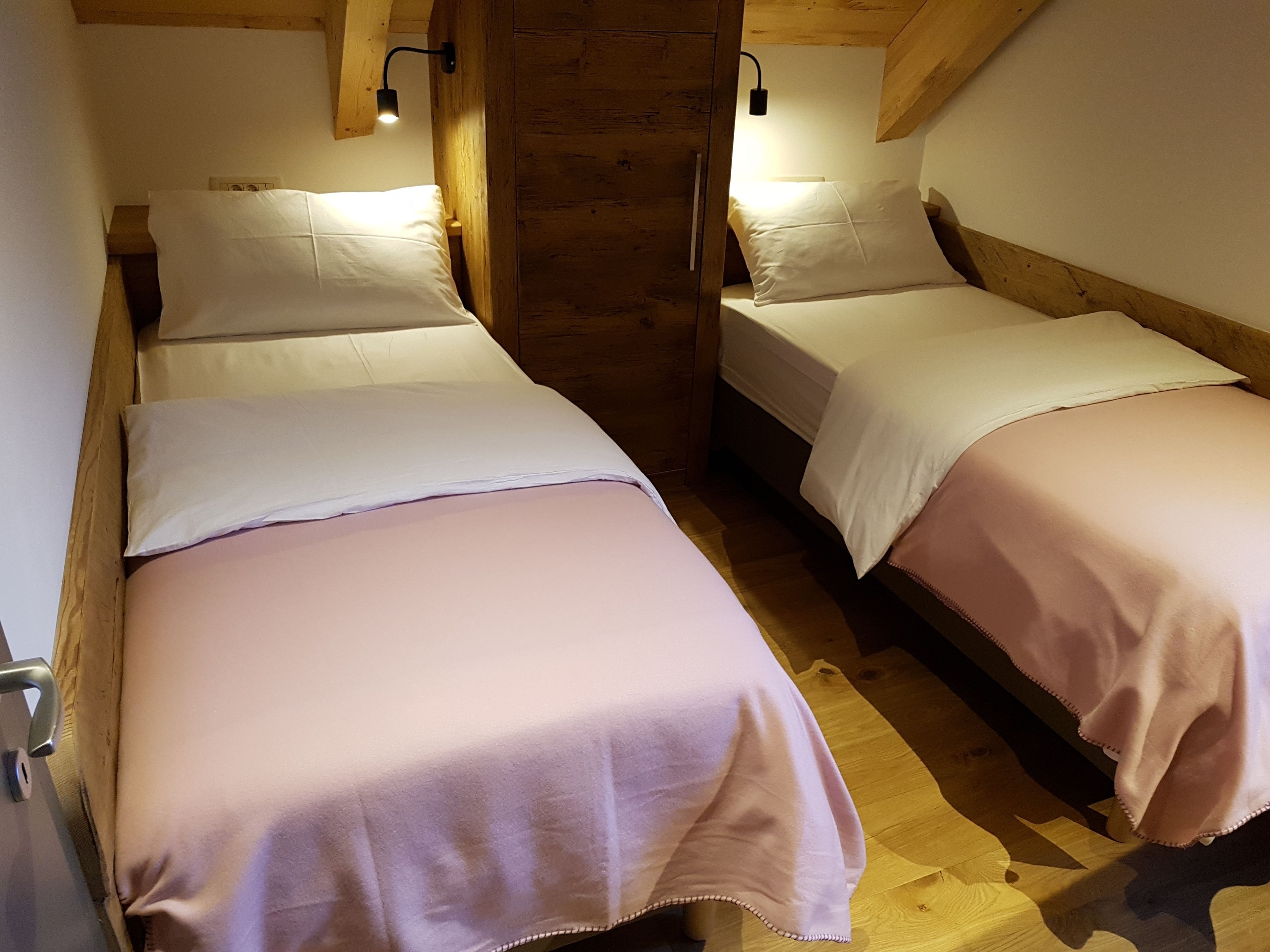 Two single beds with white linens and pink bedding, wooden beams, and a stone wall in a rustic room.