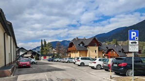 Un estacionamiento con autos, un edificio de techo inclinado y montañas al fondo.