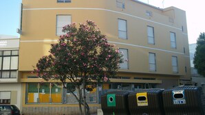 A multi-story building with a yellow facade, several windows, and a tree with pink flowers in front.