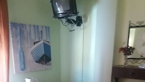 A small room with a television mounted on the wall, a small table with a polka dot tablecloth, a striped chair, and a wooden cabinet.