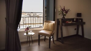 A room with a chair, a small table with a vase of flowers, a desk with a lamp, and a view of a balcony with a railing. - Piccola Navona Roof Garden (Rome)
