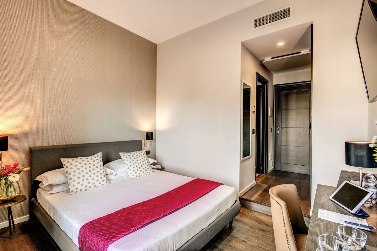 A hotel room with a large bed, a desk with a laptop, a chair, and a bathroom with a shower and toilet.