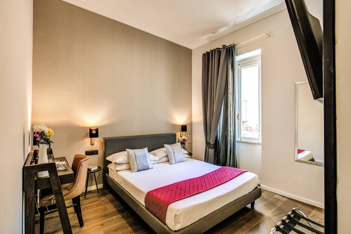 A hotel room with a bed, bedside tables, a desk, and a chair.