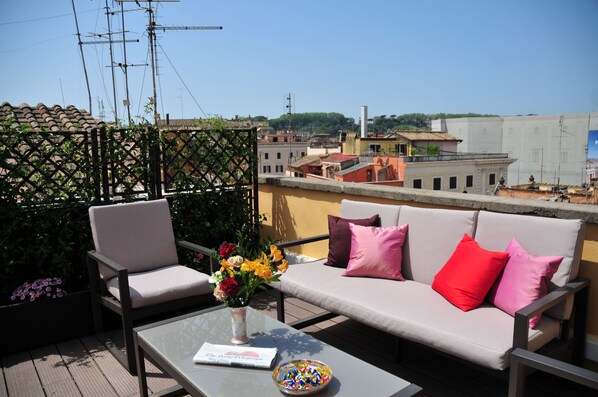 A rooftop terrace with a sofa, chairs, a table, and a vase of flowers. - Piccola Navona Roof Garden (Rome)