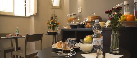A dining table with a croissant, coffee cup, milk jug, and utensils, surrounded by chairs and a vase of flowers.
