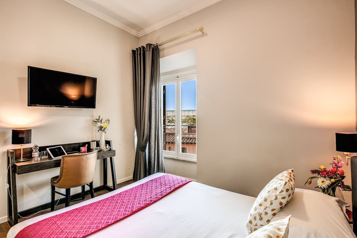 A hotel room with a bed, a desk with a laptop, a TV, and a window with curtains.