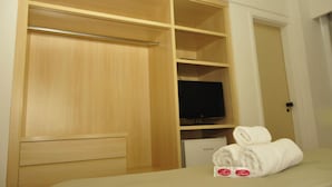 Une chambre d’hôtel avec une armoire en bois, un téléviseur à écran plat et des serviettes soigneusement pliées sur le lit.