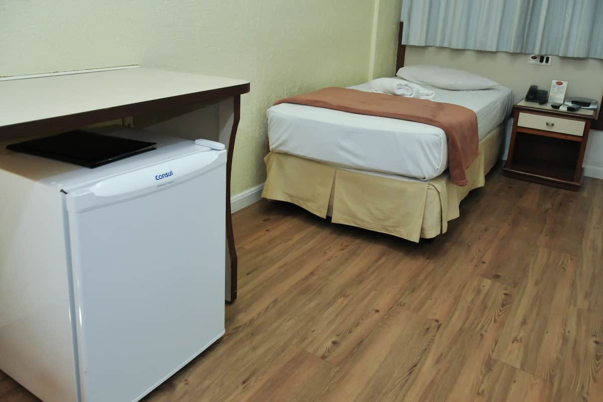 Ein kleiner, sauberer Raum mit Bett, Nachttisch und einem weißen Kühlschrank.