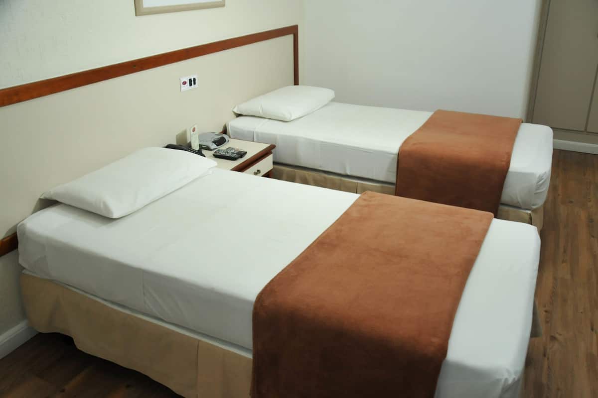 Zwei Einzelbetten mit weißen Bettwäsche und braunen Kopfteilen in einem Hotelzimmer.