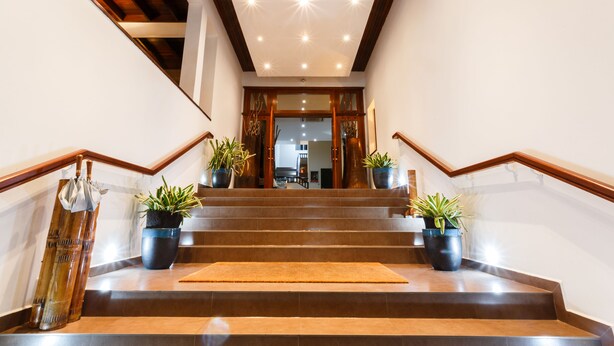 A staircase with wooden railings, potted plants, and a rug leading to an interior space. - Hotel Calypso & Spa (Toamasina)