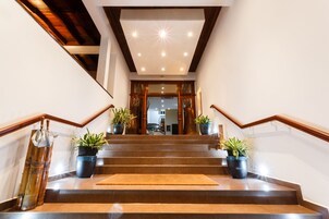 Una escalera con barandillas de madera, plantas en macetas y un tapete que conduce a un espacio interior.