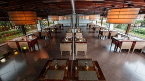 A spacious restaurant with multiple dining tables and chairs, large hanging lamps, and a view of greenery outside. - Hotel Calypso & Spa (Toamasina)