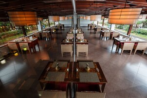 Un restaurante amplio con varias mesas y sillas, grandes lámparas colgantes y vistas a zonas verdes.