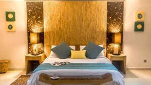 A bedroom with a bed, bedside tables, a bench, and wall art. - Hotel Calypso & Spa (Toamasina)