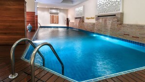 A swimming pool with a wooden deck, a glass barrier, and a wall with a decorative pattern. - Hotel Calypso & Spa (Toamasina)