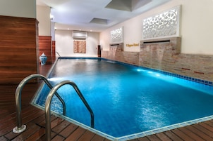 Una piscina con cubierta de madera, barandilla de cristal y pared con diseño decorativo.