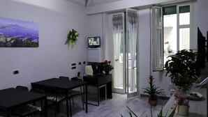 A modern dining area with a ceiling fan, a dining table with chairs, a TV, and potted plants. - Donn'Anna Bed & Breakfast (Naples)
