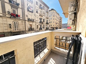 Un balcone con vista su edifici vicini, una ringhiera metallica e una finestra con inferriata.