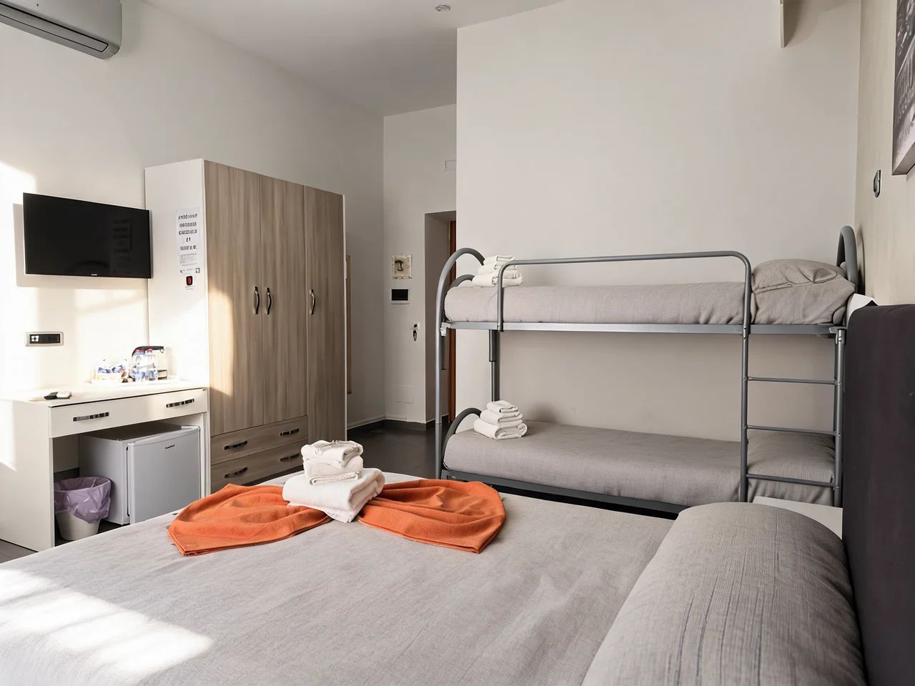 A hotel room with bunk beds, a desk with a television, and a wardrobe.