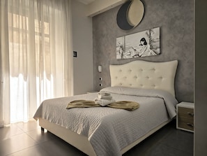 A bedroom with a bed, a bedside table, a nightstand, a wall clock, and a window with curtains. - Donn'Anna Bed & Breakfast (Naples)