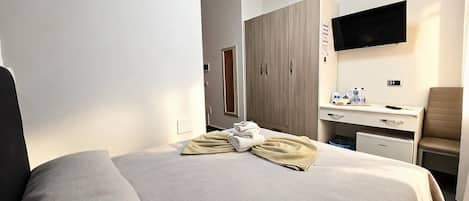 A hotel room with a bed, a desk, a chair, a television, and a wardrobe.