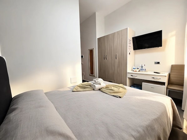 Una camera d'albergo con un letto, una scrivania, una sedia, una televisione e un armadio.