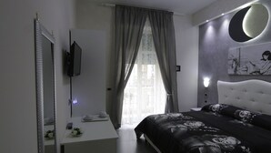 A modern bedroom with a large bed, a white bedside table, a mirror, and a wall-mounted TV. - Donn'Anna Bed & Breakfast (Naples)