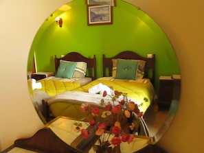 A room with two beds, a mirror reflecting the room, and a vase with flowers on a table. - Guest House Capitão Mor (Faro)