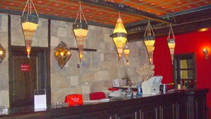 Zona de recepción con pared de piedra, faroles colgantes, pared roja y mostrador de recepción con un cartel.