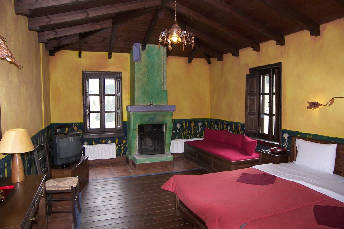 Una habitación con cama, sofá, chimenea, televisor y piso de madera.