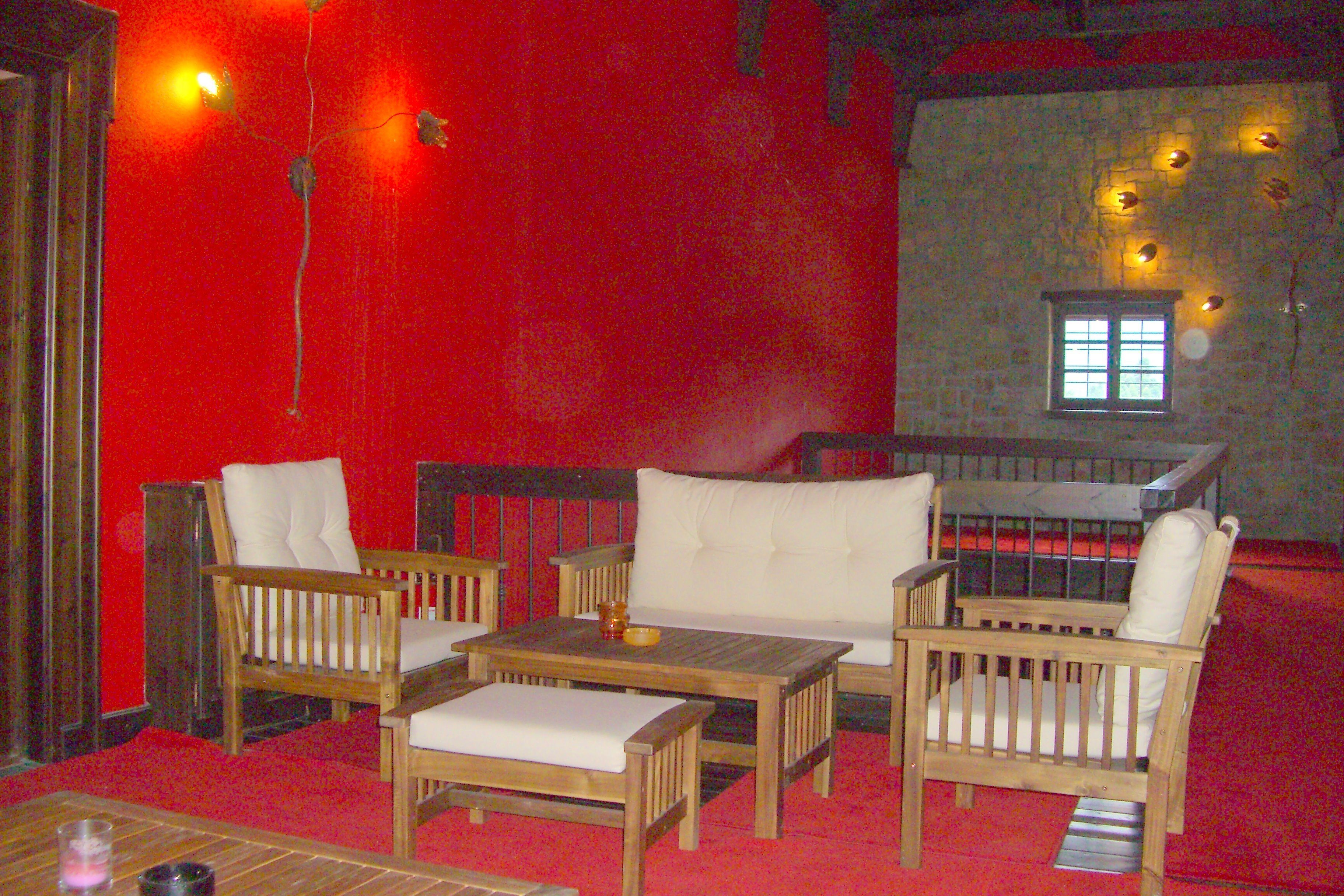 A room with red walls, wooden furniture, and a stone wall with a window.