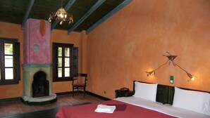 Habitación de hotel con chimenea, una cama con ropa de cama roja y dos lámparas de pared.