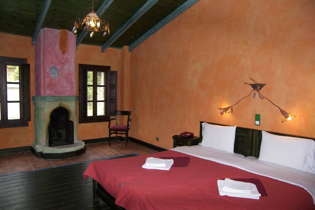 Habitación de hotel con chimenea, una cama con ropa de cama roja y dos lámparas de pared.