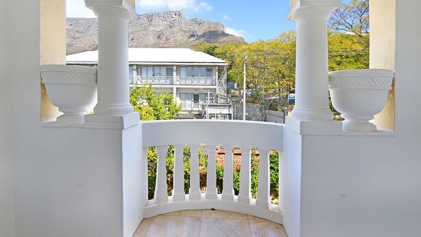 A balcony with white balustrades and columns, overlooking a building with a white roof and a mountainous backdrop. - Kenwood 7 (Cape Town)
