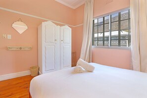 A bedroom with a bed, a window with curtains, a white wardrobe, and a wall-mounted light fixture.
