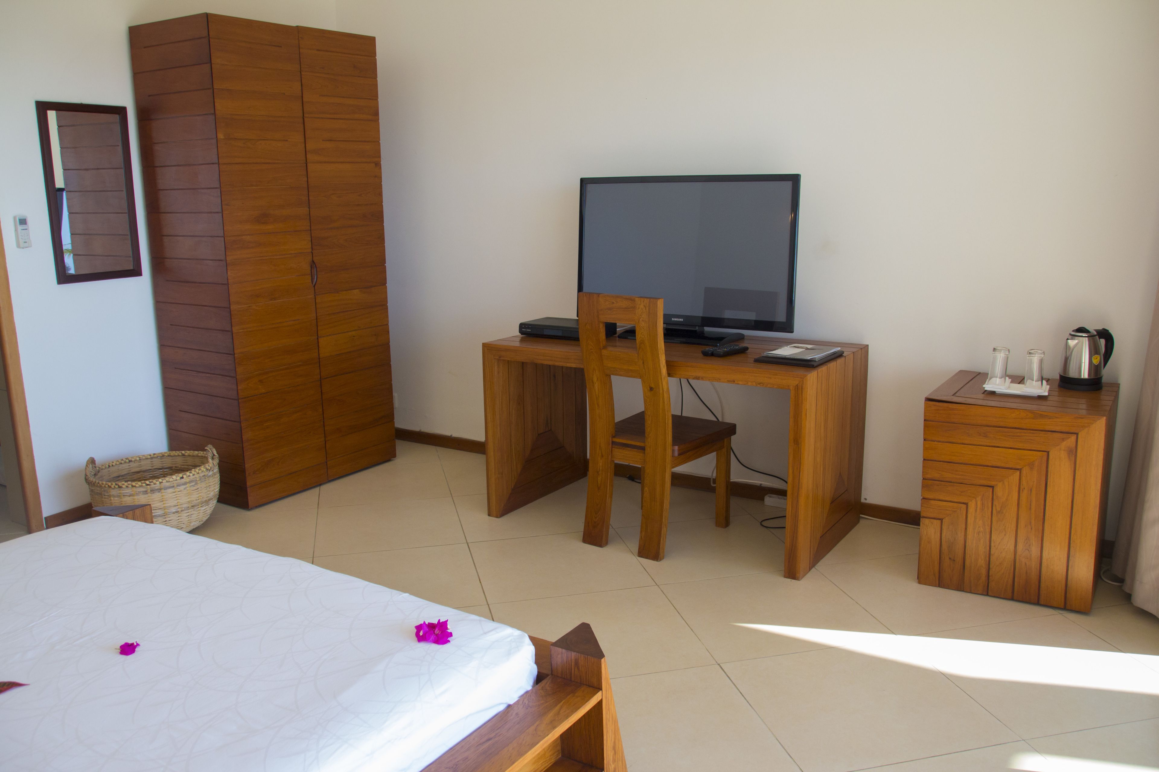 Een slaapkamer met een bed, een houten garderobe, een bureau met een televisie en een klein kastje.