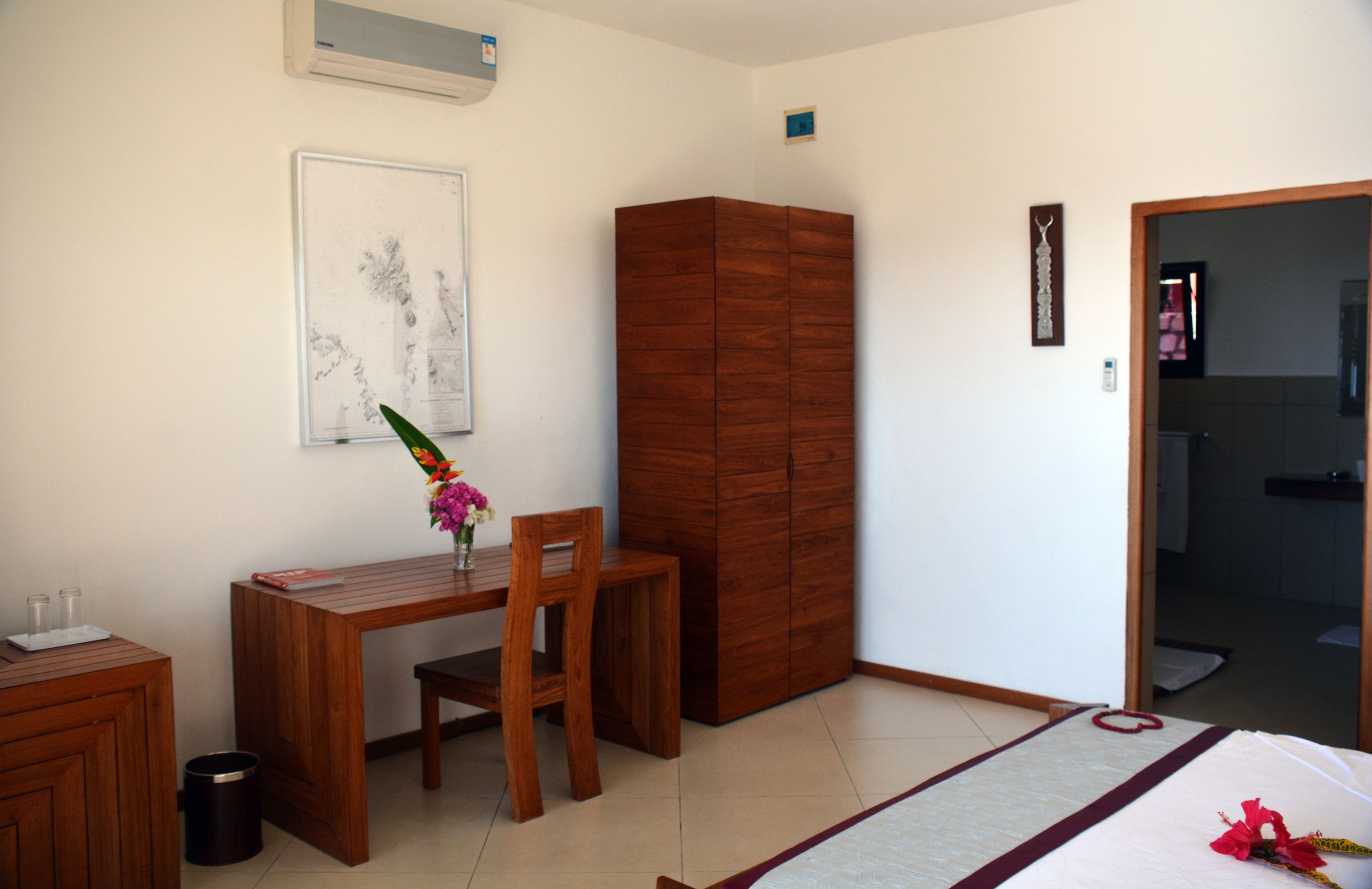 Un dormitorio con un escritorio de madera, una silla y un armario. Hay un cuadro en la pared y un cesto de basura pequeño al lado del escritorio.