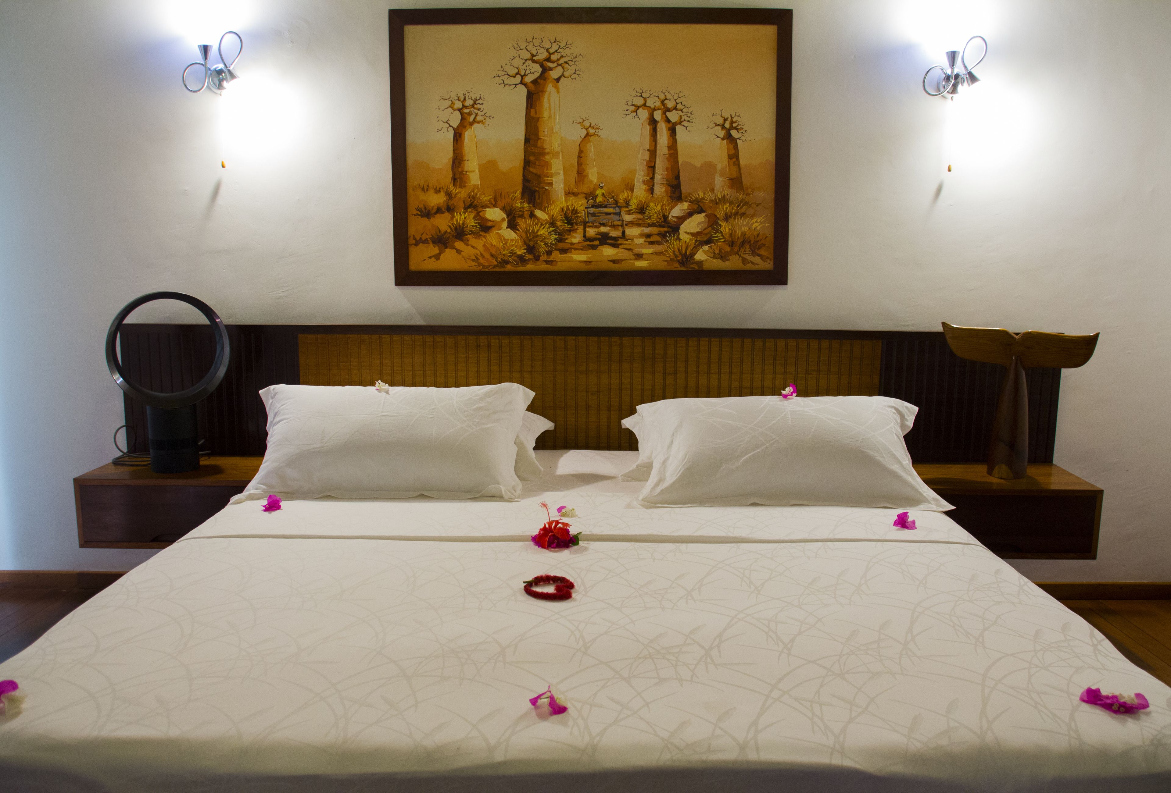 Una habitación de hotel con una cama grande, dos almohadas, una mesita de noche con lámpara y un cuadro en la pared.
