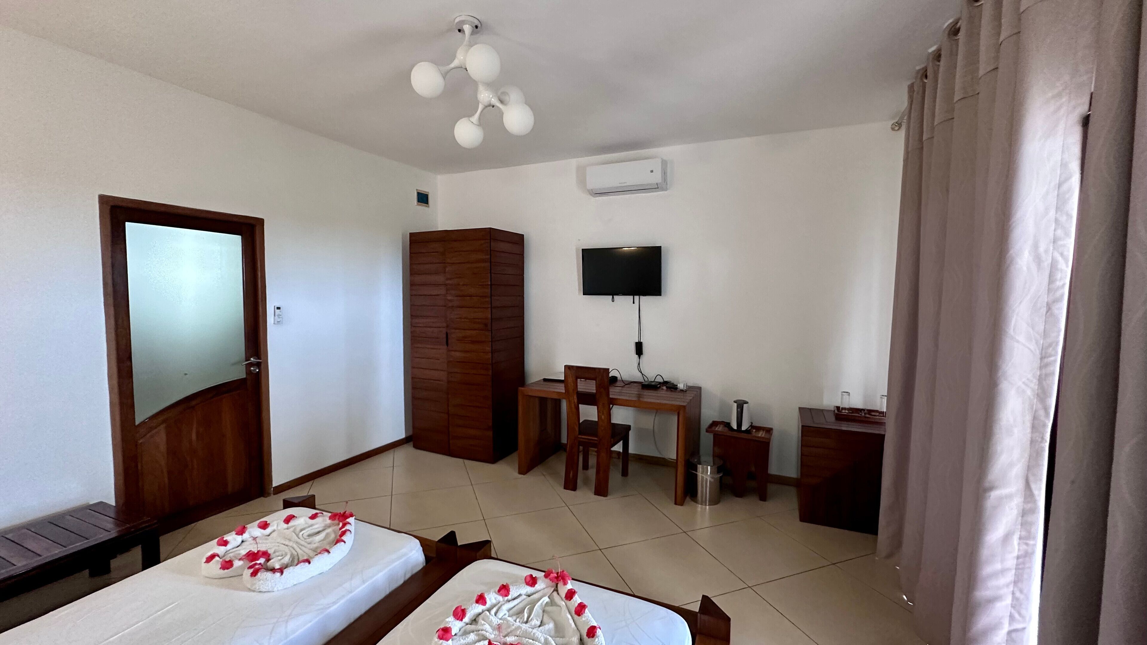 A hotel room with two beds, a desk, a chair, a TV, and an air conditioning unit.