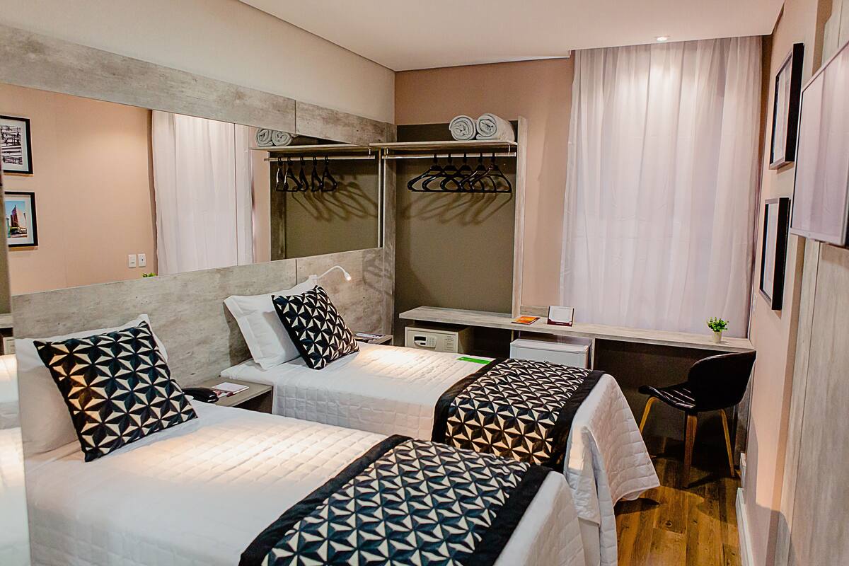 A hotel room with two beds, a desk, a chair, a mirror, and a wardrobe.