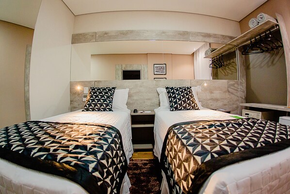 A hotel room with two beds, a small desk, a mirror, and a window with a view. - Bristol Viçosa Hotel (Vicosa)