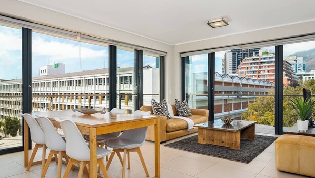 Ein modernes Wohnzimmer mit Essbereich, großen Fenstern und Blick auf Gebäude.