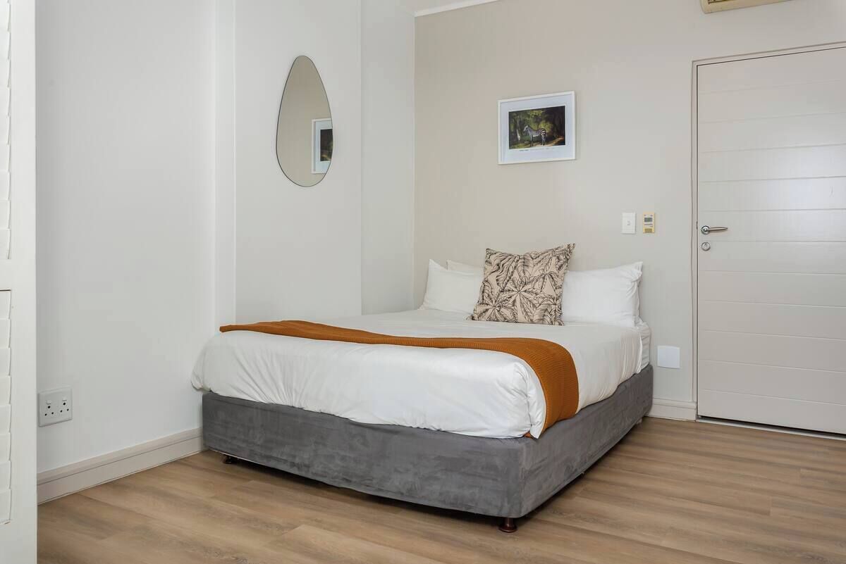 Un dormitorio con una cama, un espejo, un cuadro en la pared y una puerta.
