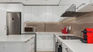 Eine moderne Küche mit weißen Schränken, einem Edelstahl-Kühlschrank, einer Mikrowelle, einer roten Kaffeemaschine und einem Geschirrspüler.