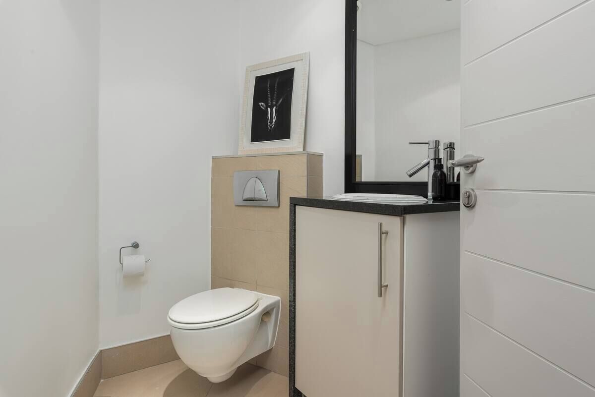 A modern bathroom with a white toilet, a sink with a black countertop, and a framed picture on the wall.